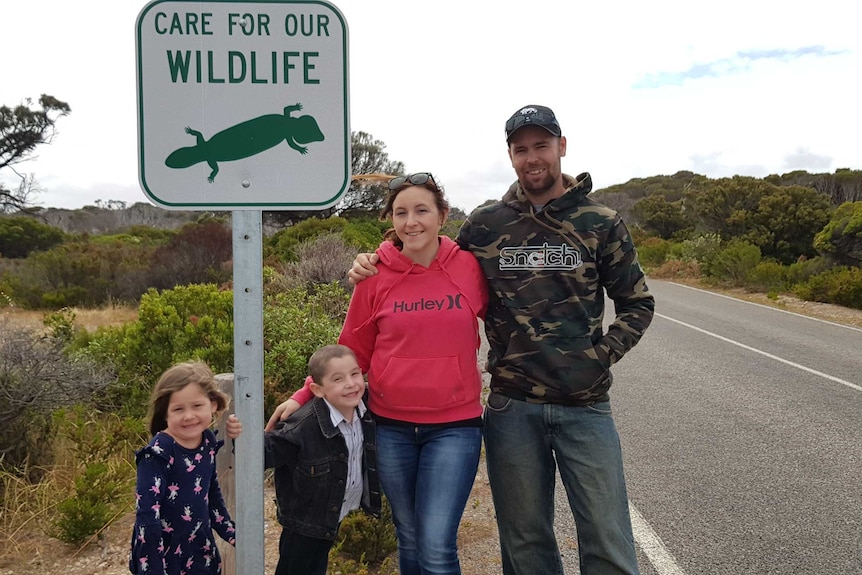 Jake Croker stands next to the road warning sign with his mum and step-dad.