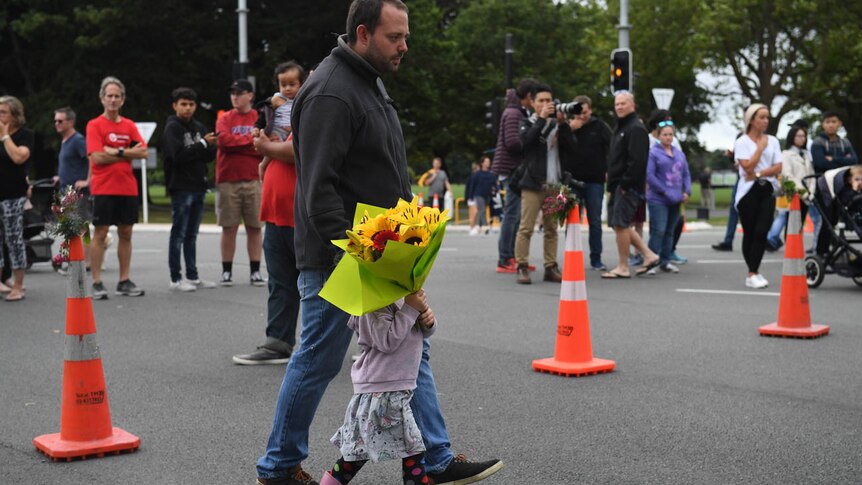 A little girl holding flowers walks with her father towards a memorial on Dean's Avenue in Christchurch.