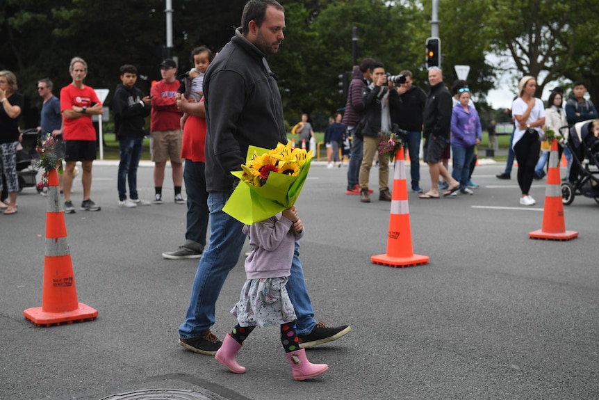 A little girl holding flowers walks with her father towards a memorial on Dean's Avenue in Christchurch.