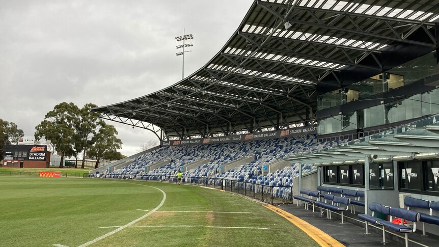 An empty grandstand next to a football oval on a cloudy day.