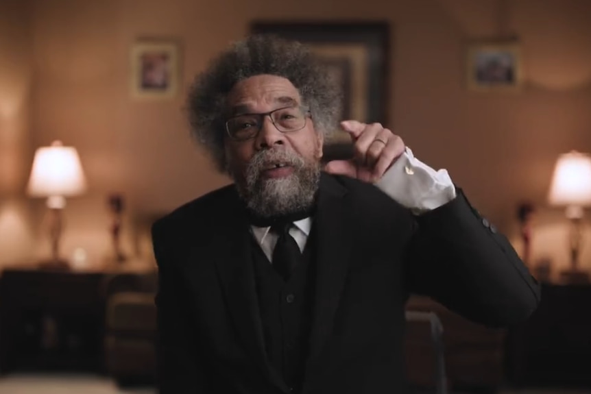 An older black man with a beard and grey frizzy hair gestures as he speaks to the camera in a tastefully lit room.