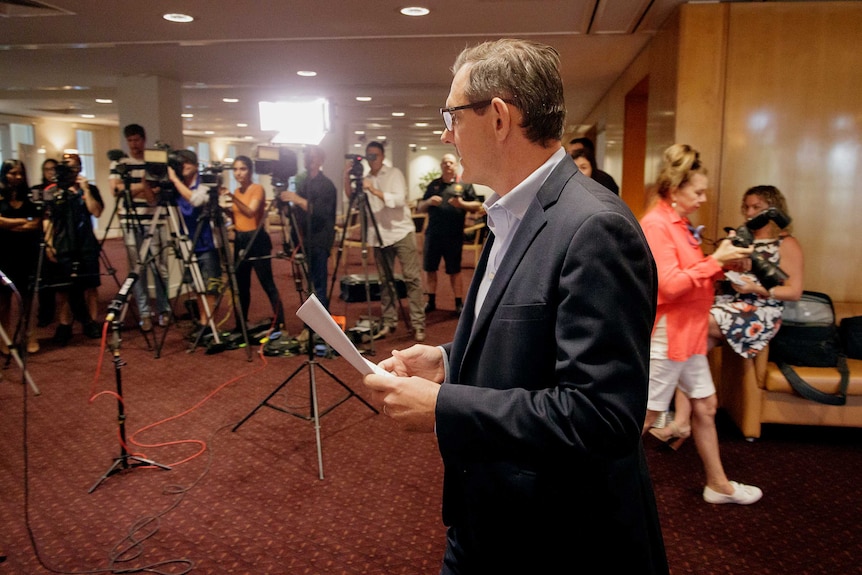 A side-on photo of NT Chief Minister Michael Gunner at a press conference with media in background