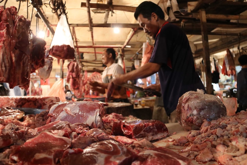 A bench covered in beef and buffalo meat with a butcher in the background in the wet market.