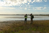 Two hunters standing in wetlands near a lake.