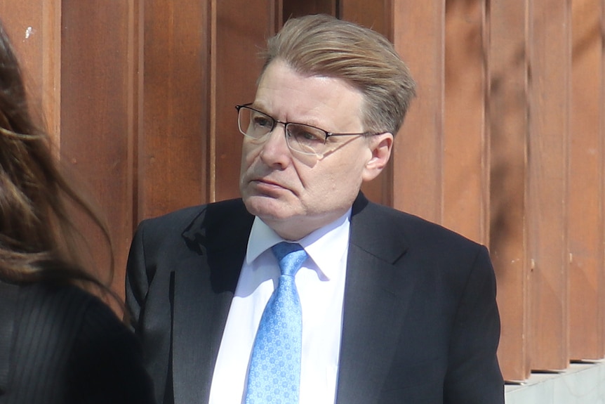A head and shoulders shot of WA Ombudsman Chris Field walking outside wearing a dark suit, blue tie, white shirt and spectacles.