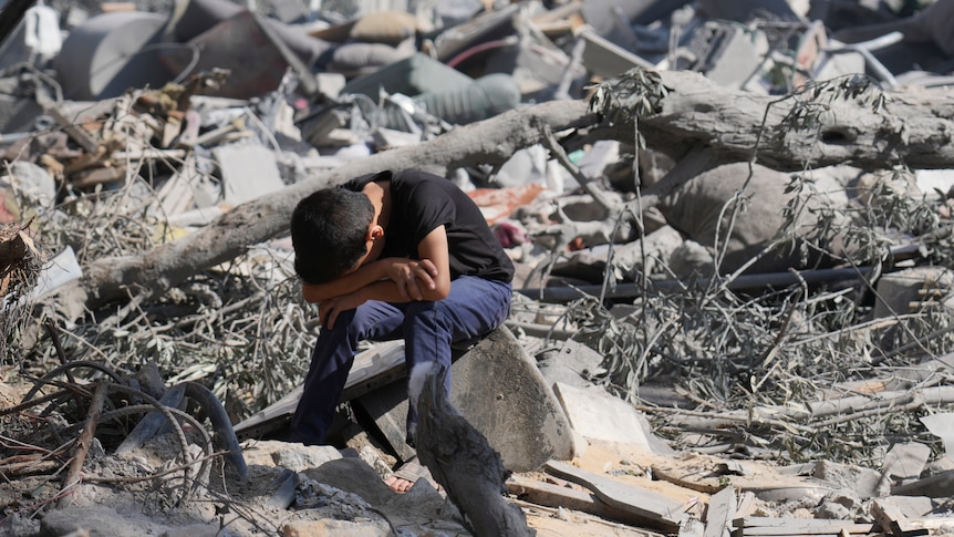 A Palestinian boy sits on the rubble of the building destroyed in an Israeli airstrike.