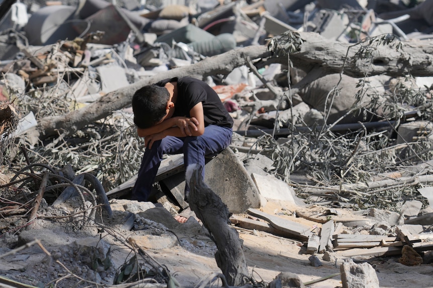 A Palestinian boy sits on the rubble of the building destroyed in an Israeli airstrike.