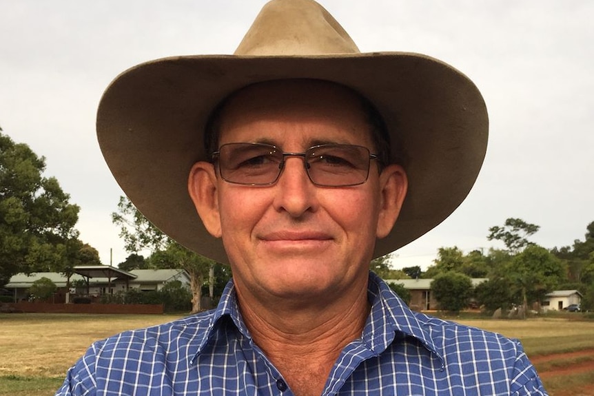 A rural-looking man wearing an outback hat and glasses smiles at a camera.