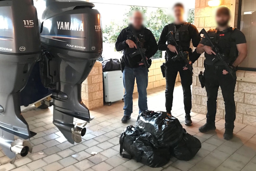 Three AFP officers dressed in black and carrying guns stand at the back of a boat outside a house with packages on the ground.