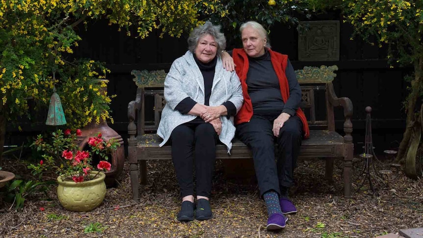 Hilary and Kristin sit on a bench surrounded by their colourful garden.