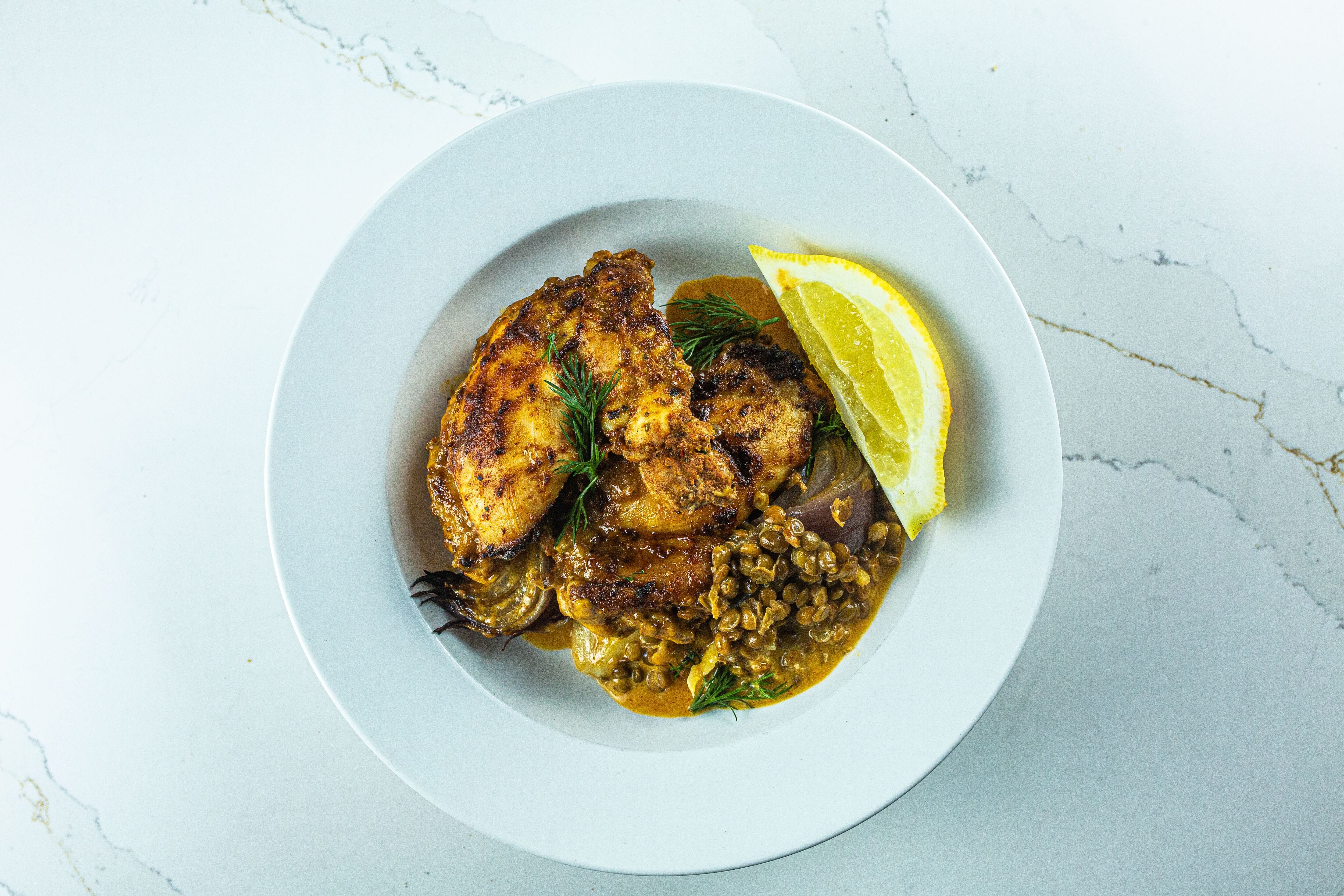 An individual serving of chicken and lentil tray bake in a bowl with lemon wedges and dill.