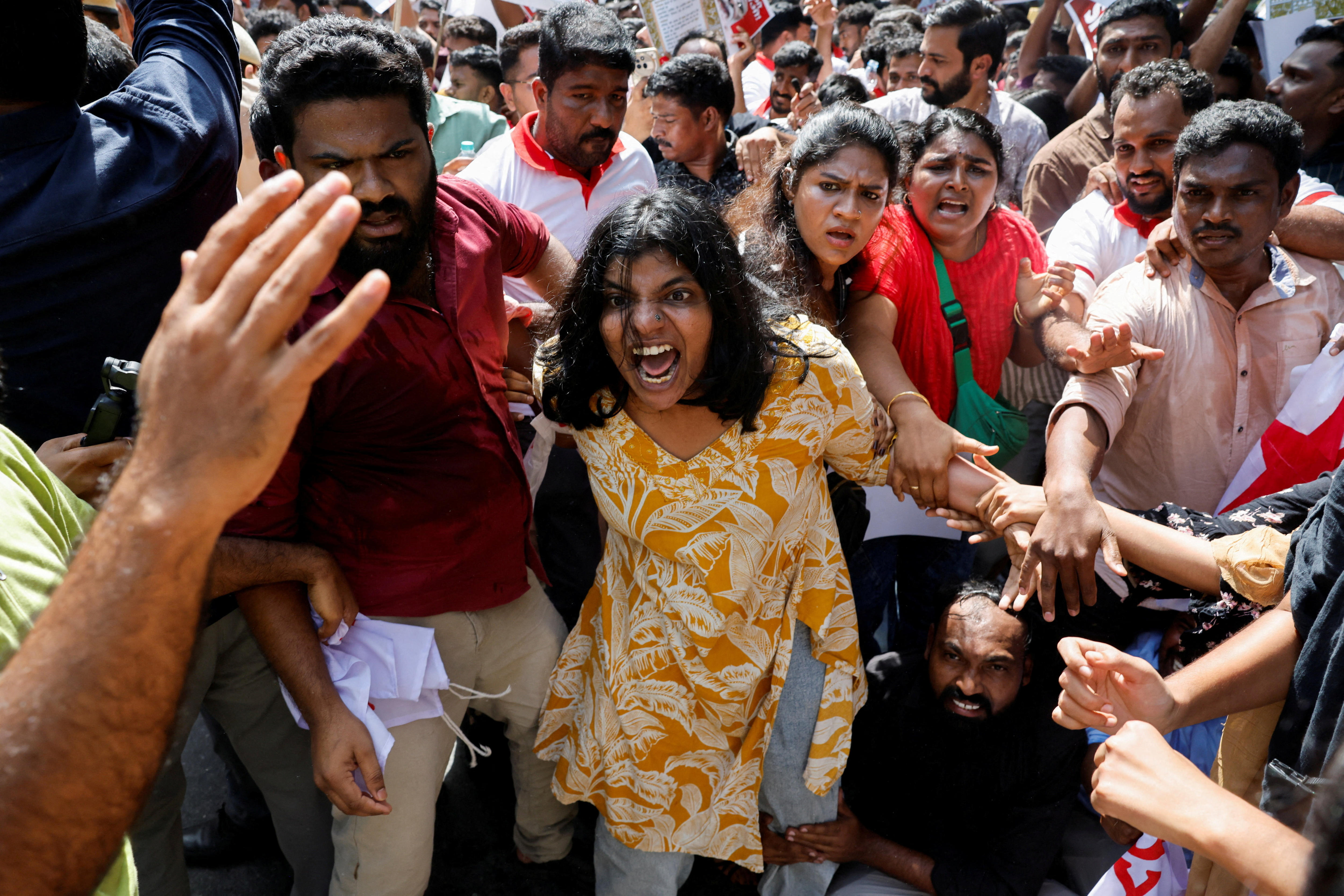A woman in a pink dress grimaces as hands from a crowd are seen grabbing her arms.
