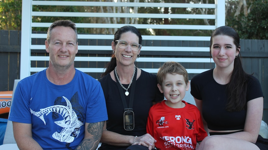 Heath family smiling on lounge with white pergola and fence in background