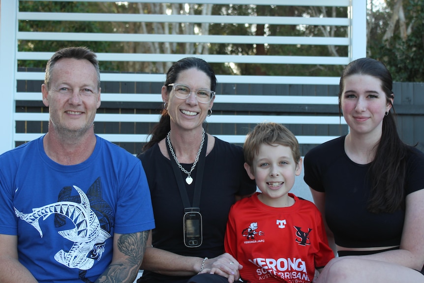 Heath family smiling on lounge with white pergola and fence in background