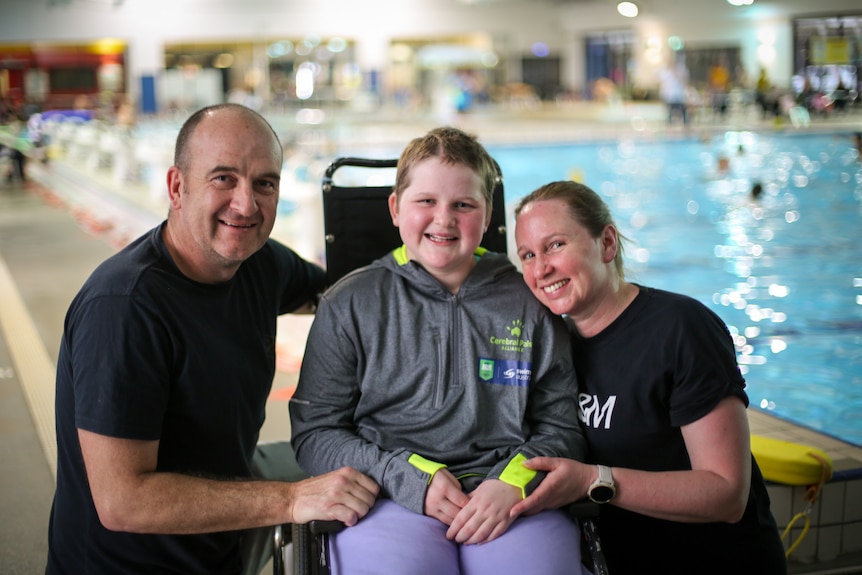 Mackenzie Miller dans son fauteuil roulant entre ses parents au Orange Aquatic Center