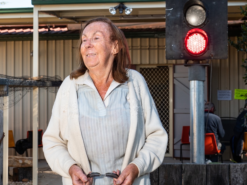 A woman standing in front of a train signal shining a red light.