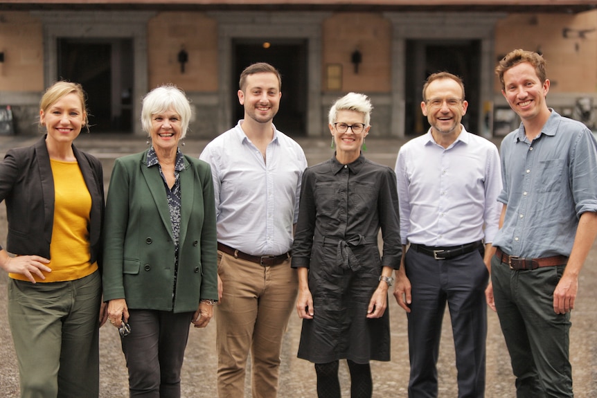 The greens team stand in a line smiling.