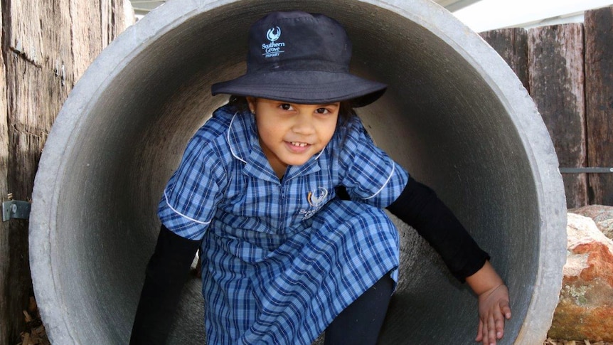 A student is crouched down in a large cement cylinder in the playground.
