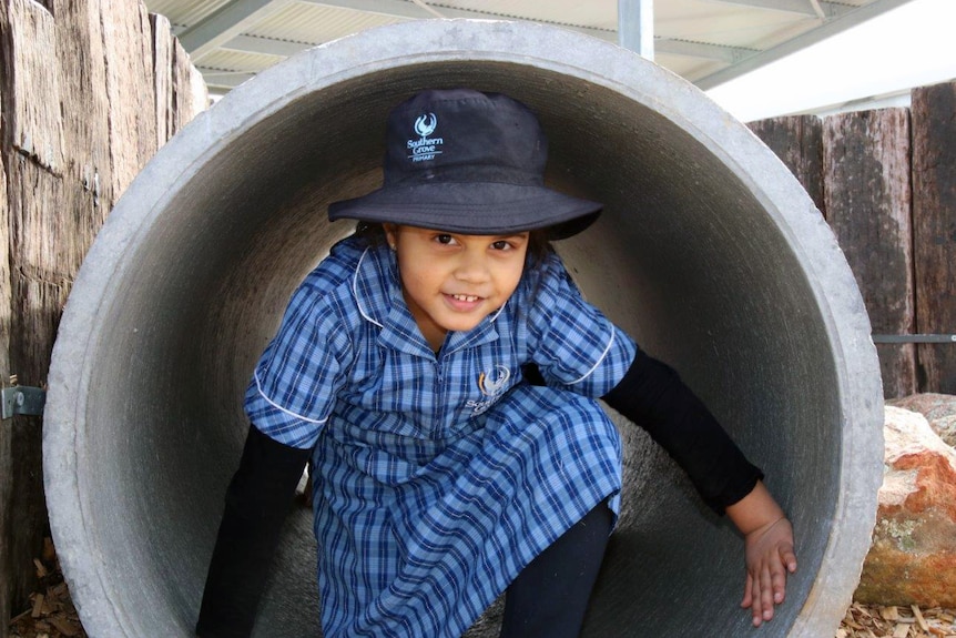 A student is crouched down in a large cement cylinder in the playground.