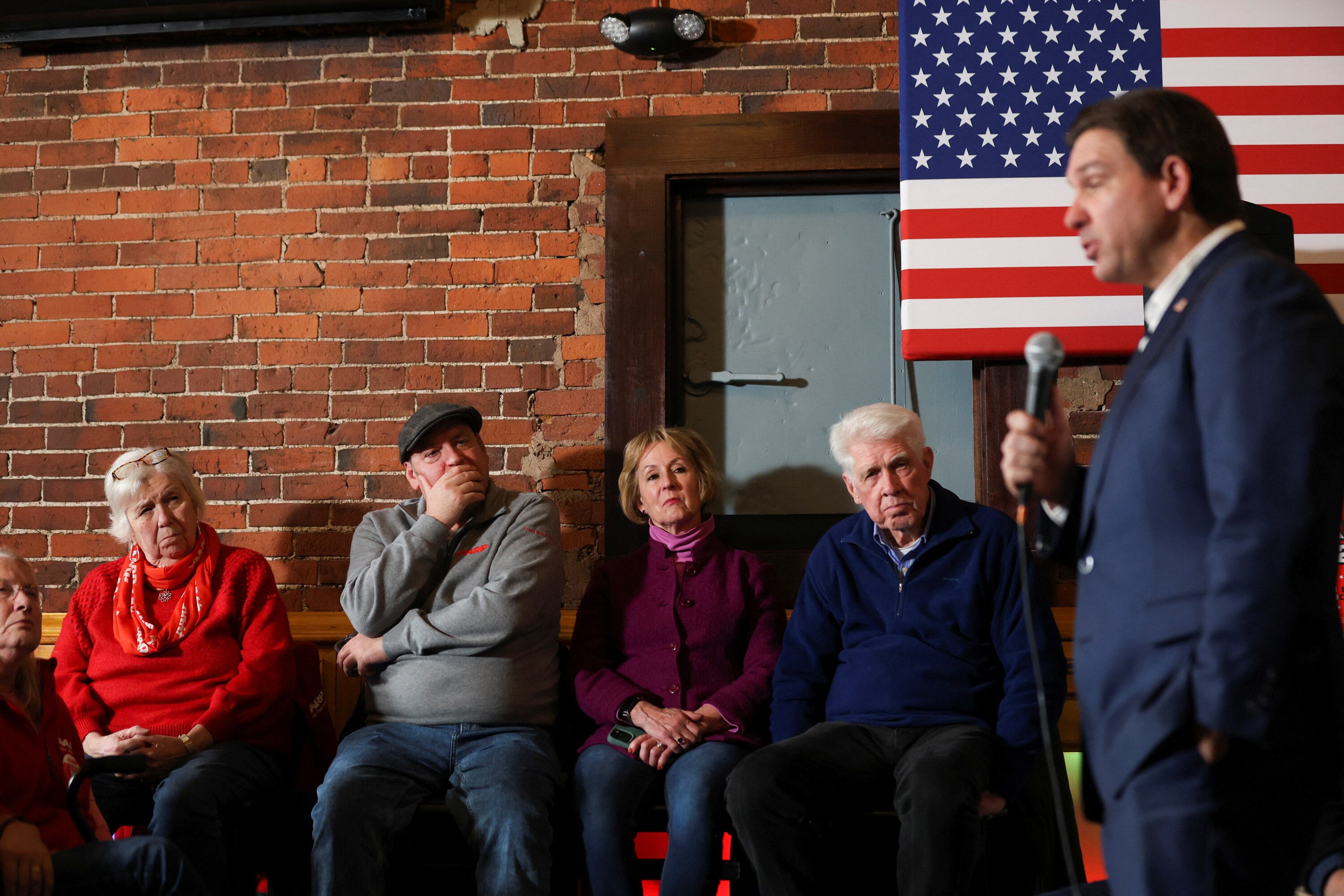 Ron DeSantis talks into a microphone in front of a crowd of people watching on.
