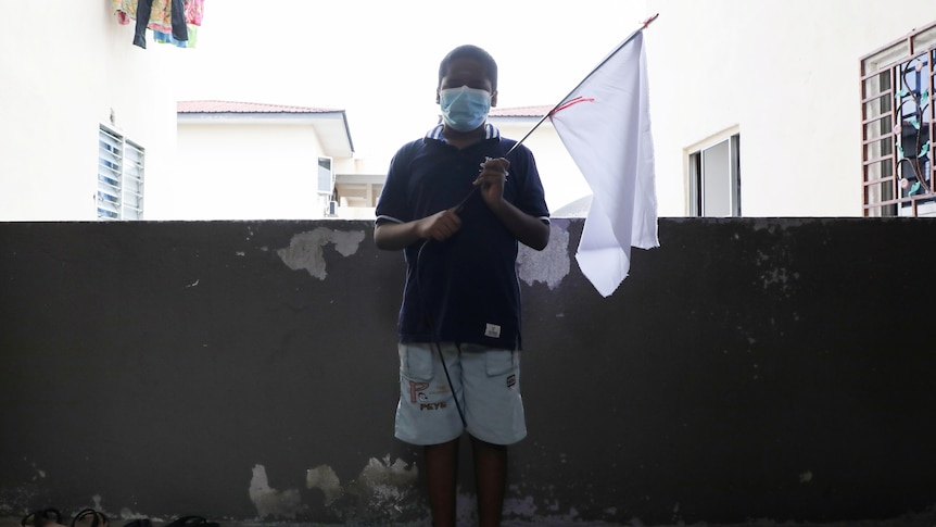 A boy holds a white flag which his family hung to ask for help
