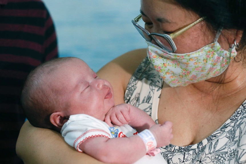 Woman with mask holds a newborn baby.