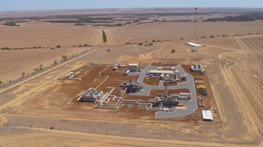 An aerial view of a compressor station featuring various buildings and pipelines in a rural field.