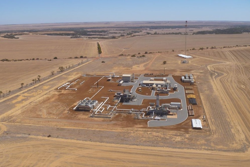 An aerial view of a compressor station featuring various buildings and pipelines in a rural field.