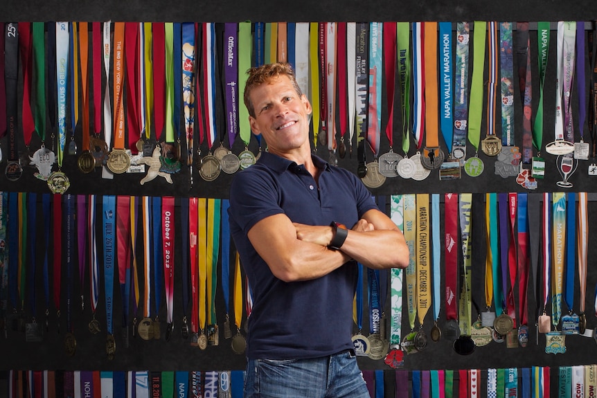 Dean Karnazes stands in front of a wall of his medals.
