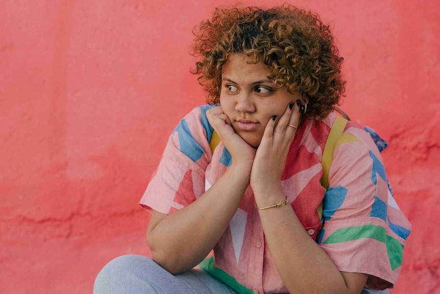 Young woman in bright colours looking thoughtful but also slightly fed up and angry