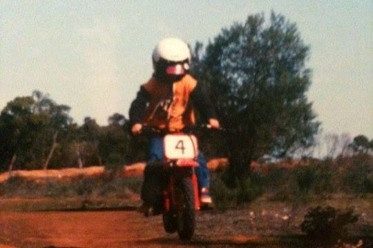 A boy on a motorbike with a helmet on riding on a red dirt track