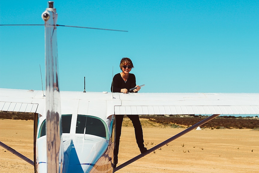 A woman smiles as she stands on the wing of a light aircraft holding a tool.