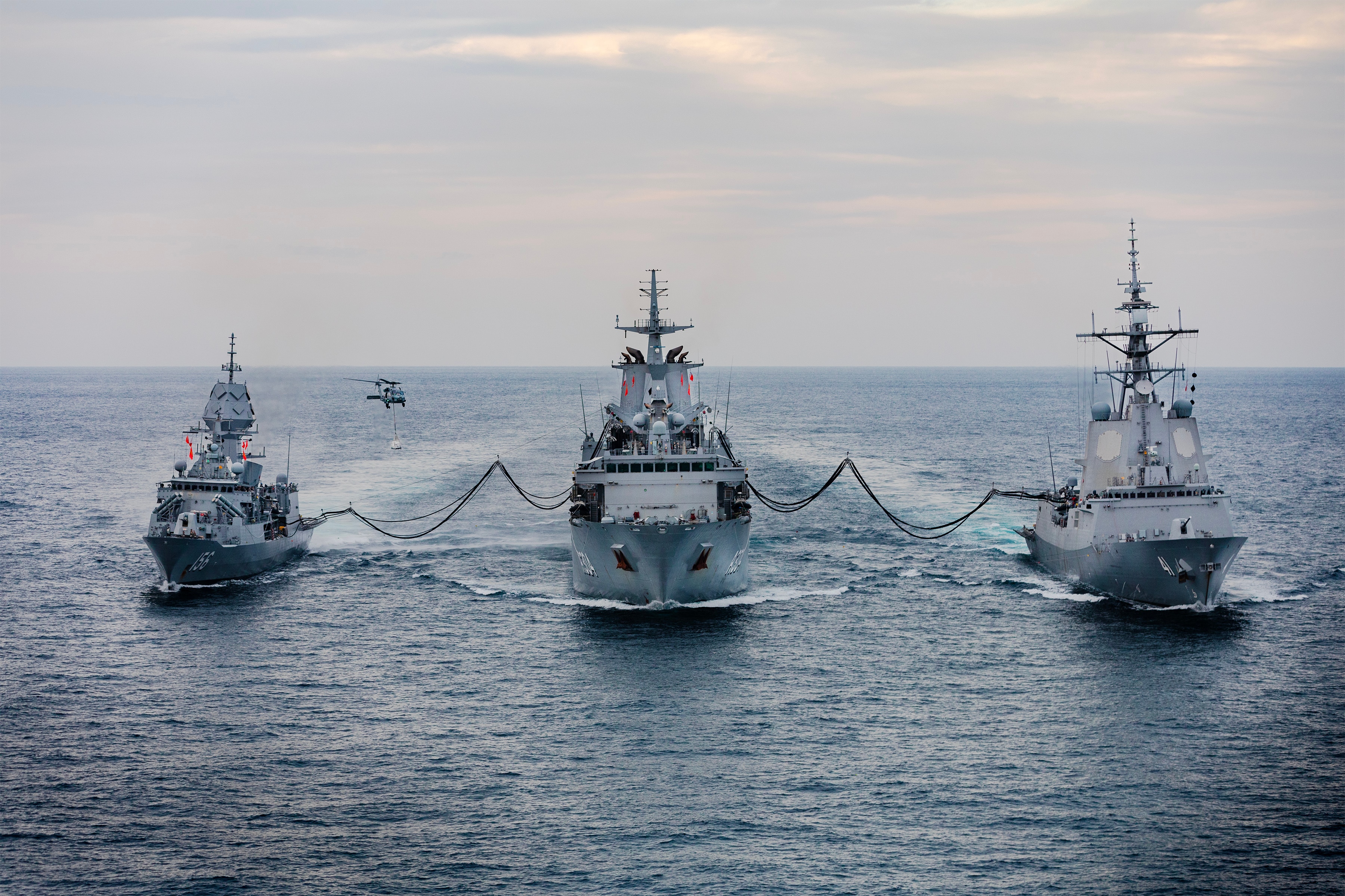 Three ships line up in open waters with refueling lines connecting them.