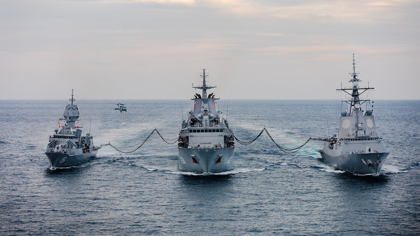 Three ships line up in open waters with refueling lines connecting them.