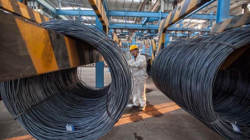 An employee inspects newly-made steel coils at a steel plant in Lianyungang, Jiangsu province