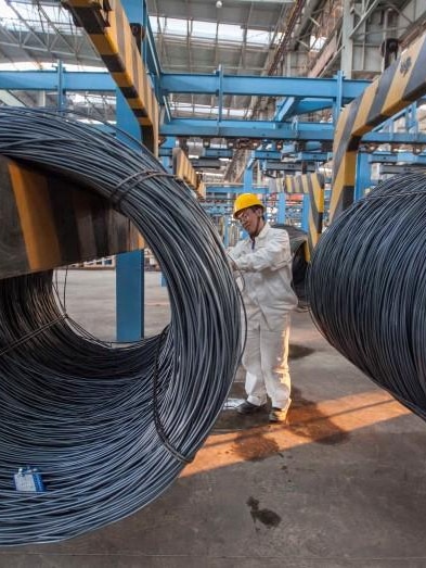 An employee inspects newly-made steel coils at a steel plant in Lianyungang, Jiangsu province