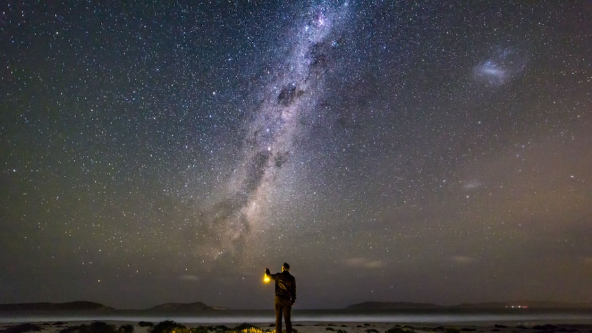 A man holding a lantern standing on a beach, with a starry sky above.