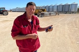 A man in a red shirt standing on a farm with a mobile phone in hand.