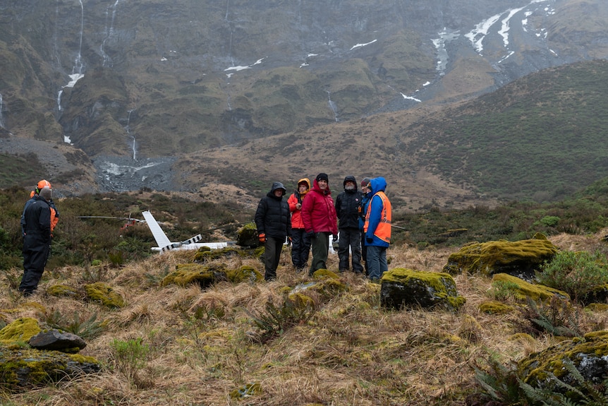 A group of people stand in the valley floor surrounded by mountains 