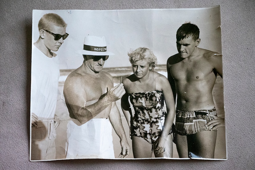 A black and white photo of three men and a woman at the beach in the1950s
