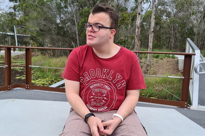 young man sitting on a bench with gum trees behind him