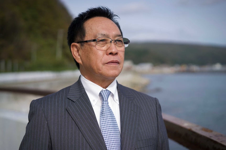 A profile shot of Takumi Shinmura wearing a suit looking into the distance