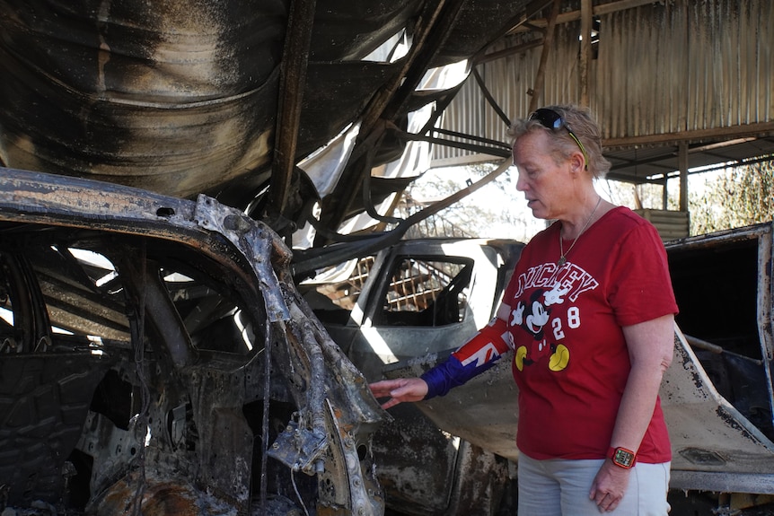 A woman inspects a burnt car in a shed