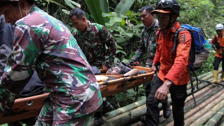 Resuers carry a man on a stretcher through trees on the island of Sumatra.