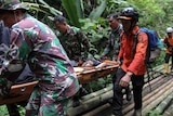 Resuers carry a man on a stretcher through trees on the island of Sumatra.