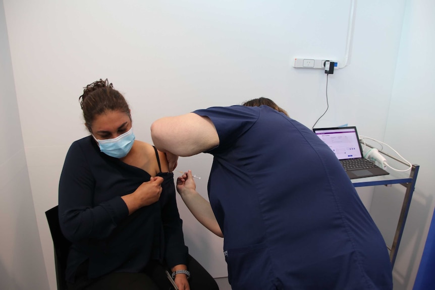 A nurse wearing a face mask receives a coronavirus vaccine from another nurse with their back to the camera.