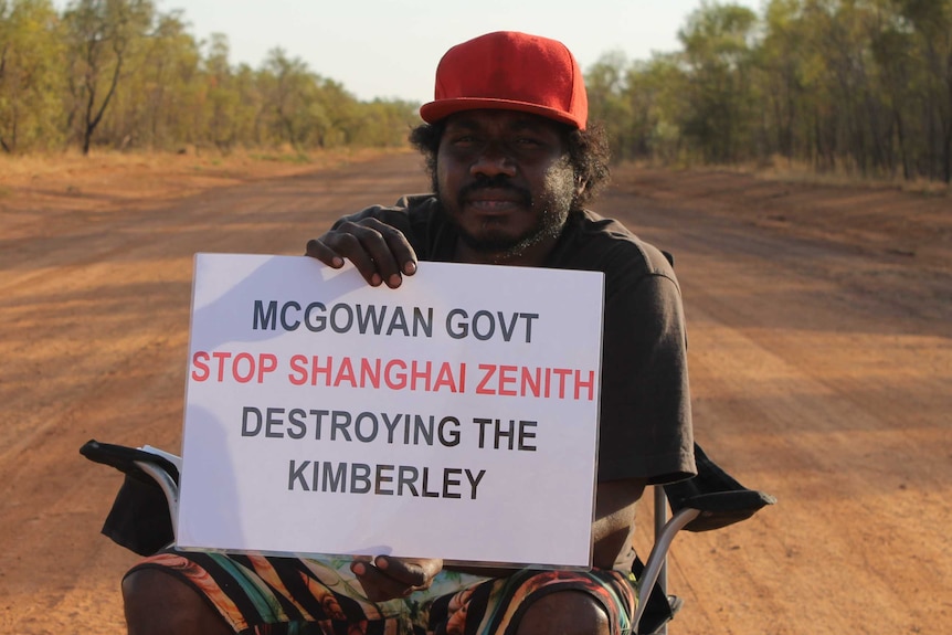 man in red cap holding up sign, sitting on chair in middle of dirt road