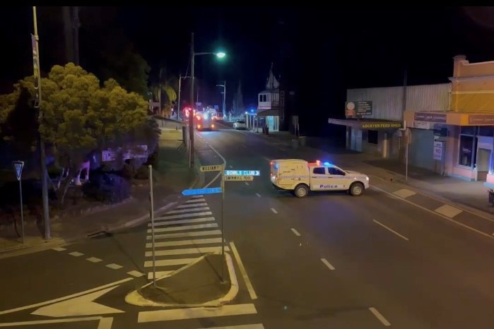 A police panel van parked across a dark street. A fire truck is visible further down the road.