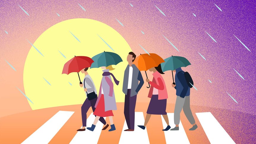 A man without an umbrella stands on a pedestrian crossing facing the rain while others with umbrellas pass him by.