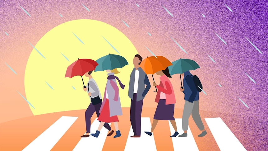 A man without an umbrella stands on a pedestrian crossing facing the rain while others with umbrellas pass him by.